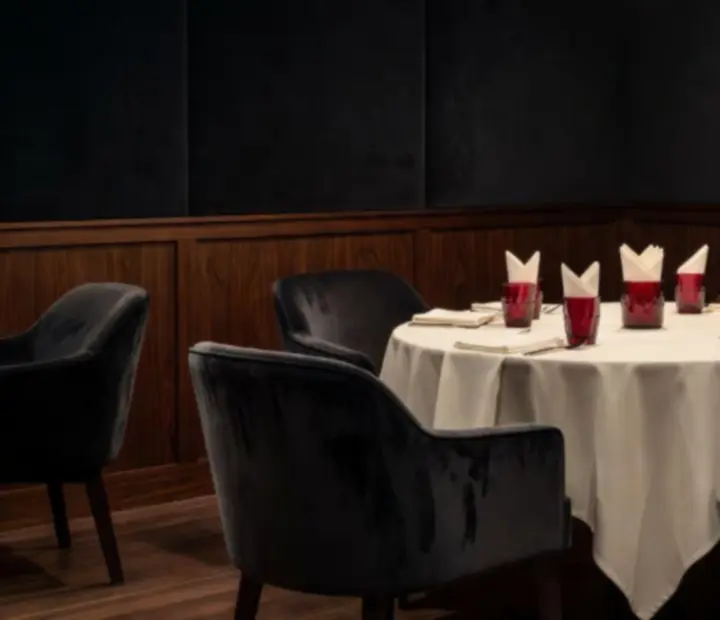 Atmospheric lounge room with deep navy drapery, walnut tabletops and warm lamp lighting